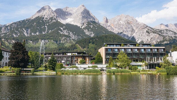 A hotel with a view of mountains, a lake, and outdoor seating.