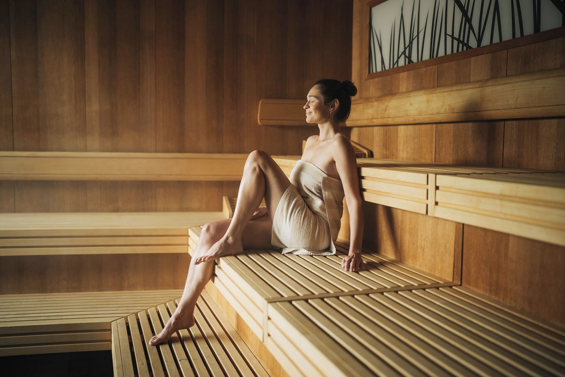 A person sitting on a wooden bench in a sauna with a wooden wall and a framed picture.