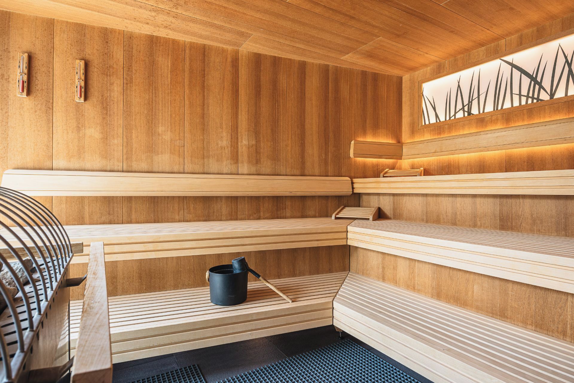 Una sauna con bancos de madera, un cubo negro y un calentador fijado a la pared.