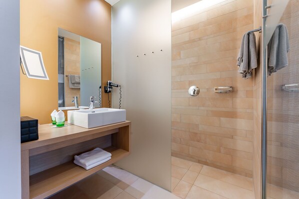 A modern bathroom with a large mirror, a white sink, and a glass-enclosed shower.