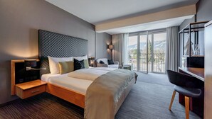 A modern hotel room with a large bed, a desk, and a view of the outdoors. - Ritzenhof – Hotel und Spa am See (Saalfelden am Steinernen Meer)