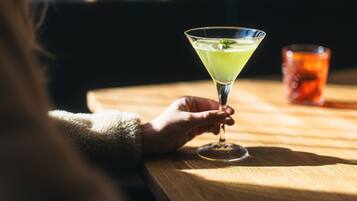 Una mano sostiene una copa de martini con una bebida verde sobre una mesa de madera.