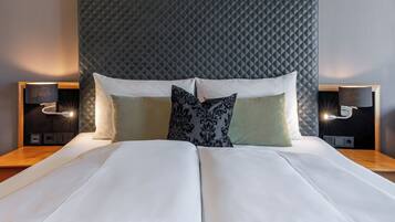 Una cama bien hecha con un cabecero acolchado, dos lámparas de noche y un plaid verde al pie de la cama.