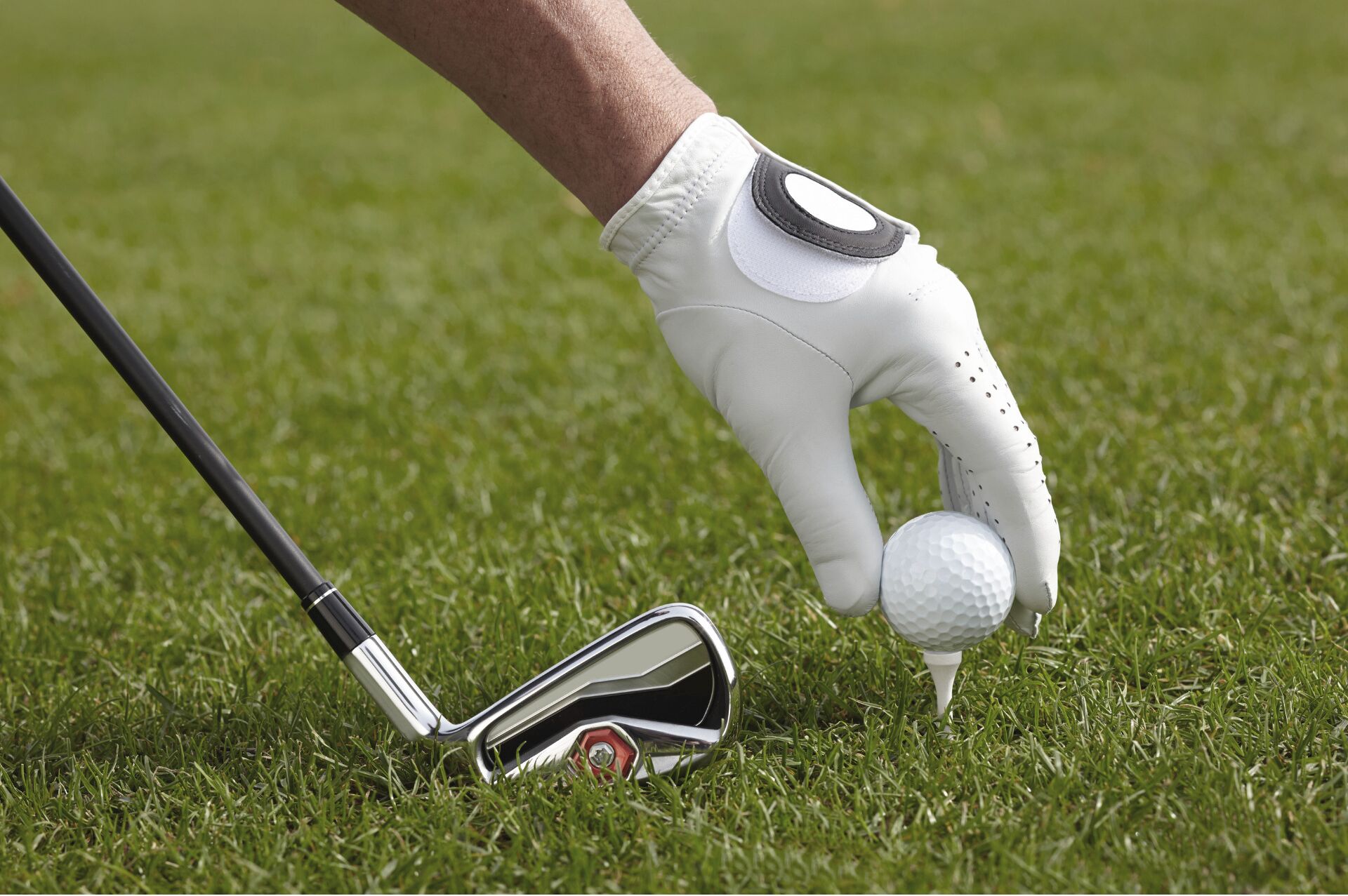 A golf club with a white grip and a golf ball on a green field.