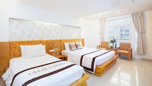 Habitación de hotel con dos camas, cabecera de madera, ventana grande con cortinas y mesita de noche con un florero.