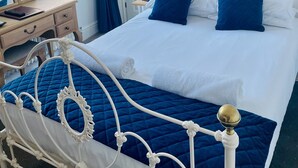 A neatly made bed with blue bedding and a white metal frame, a bedside table with a lamp, and a framed picture on the wall. - Canterbury Hotel (Canterbury)