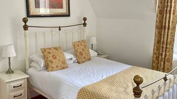 A neatly made bed with white bedding and patterned pillows, a bedside table with a lamp, and a framed picture on the wall.