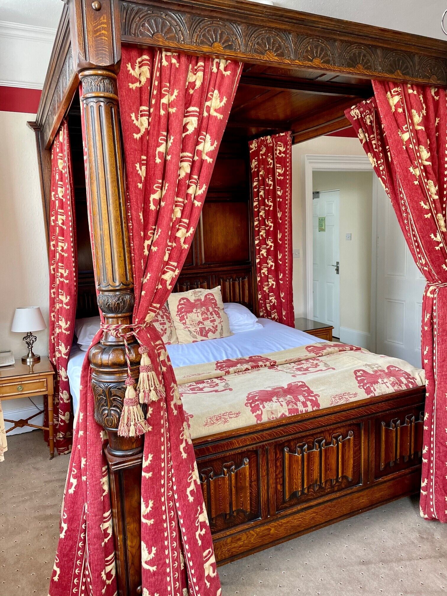 A four-poster canopy bed with red and gold patterned curtains, a wooden headboard, and a matching canopy.