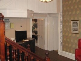 Un vestíbulo de hotel con una escalera de madera, un mostrador de recepción y una pared con papel tapiz floral.