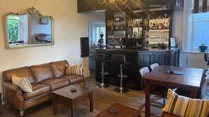 A living room with a leather sofa, a wooden coffee table, and a dining table with chairs. A kitchen area with a bar and shelves of bottles is visible in the background. - Canterbury Hotel (Canterbury)