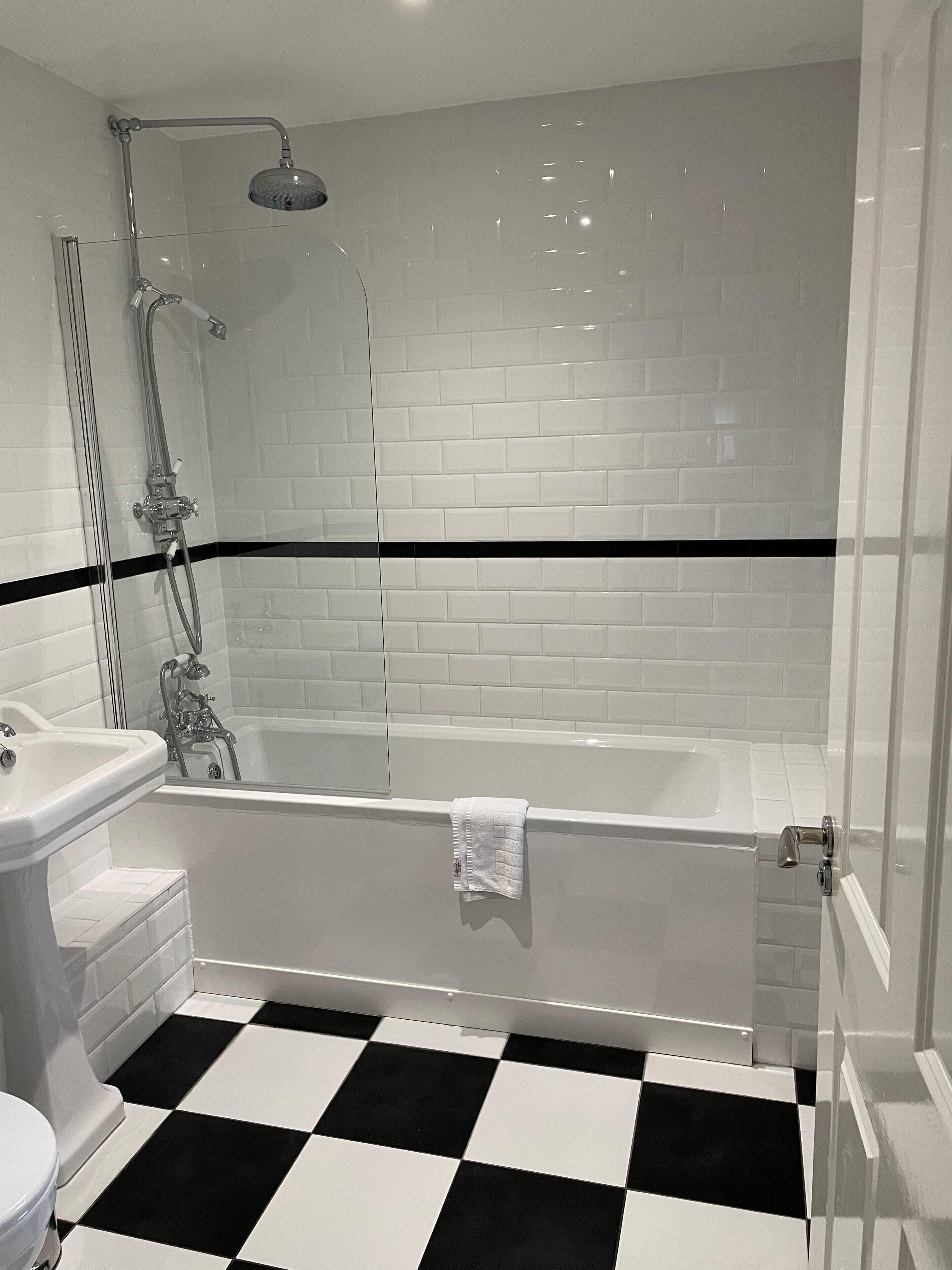 A bathroom with a white bathtub, a glass-enclosed shower, and a black and white checkered floor.