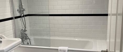 A bathroom with a white bathtub, a glass-enclosed shower, and a black and white checkered floor.