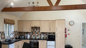 A modern kitchen with wooden cabinets, a black countertop, a microwave, an oven, and a refrigerator. There is a dining table with chairs and a clock on the wall. - Canterbury Hotel (Canterbury)