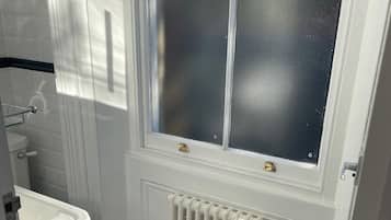 Une salle de bain avec un radiateur blanc, des toilettes blanches et une fenêtre à vitres dépolies.