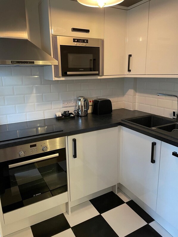 Una cocina moderna con armarios blancos, un horno Bosch, un microondas y un piso a cuadros blanco y negro.