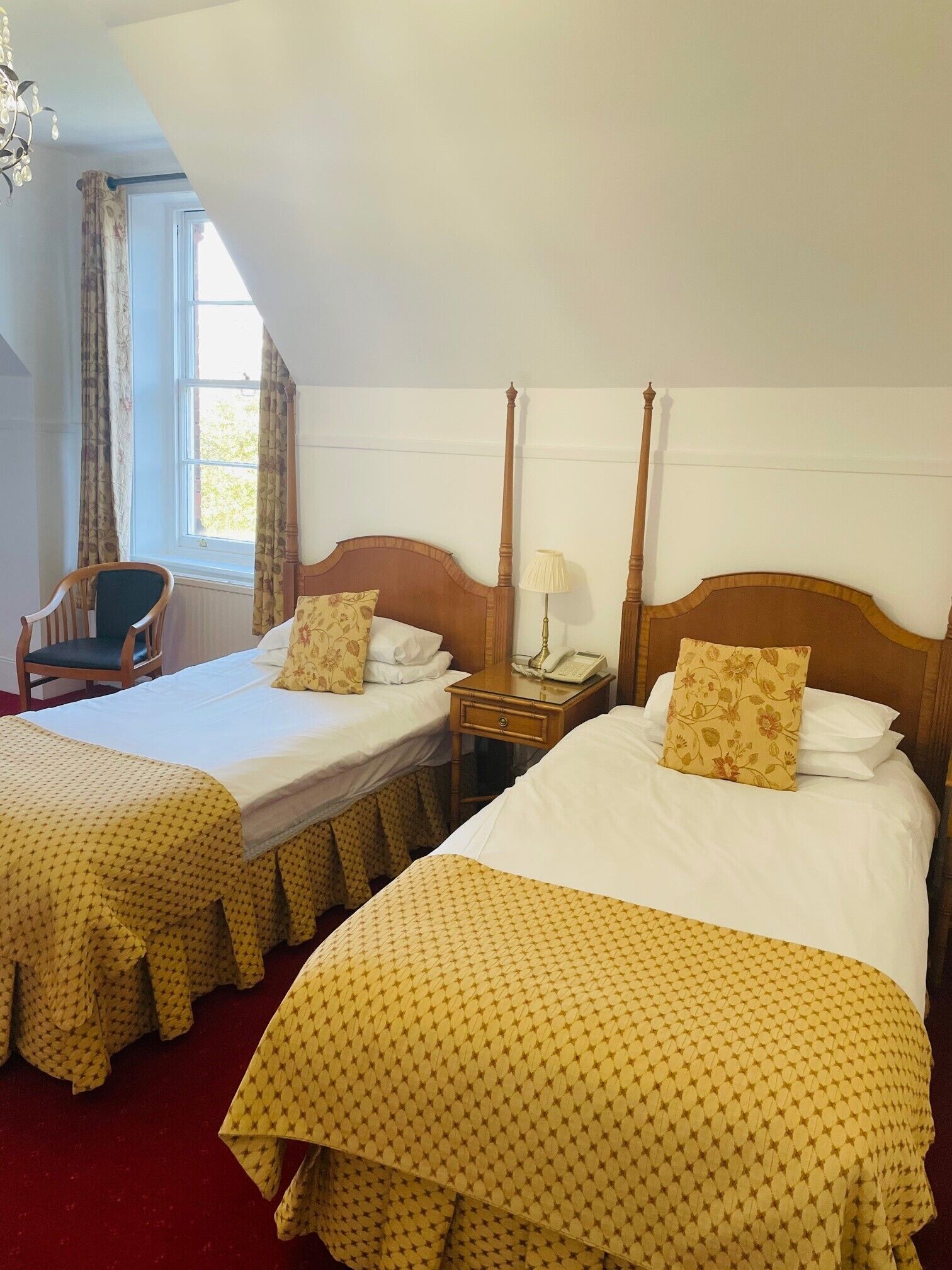 A hotel room with two beds, a chair, a nightstand with a lamp, and a window with curtains.