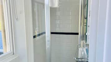 Um banheiro moderno com chuveiro em box de vidro, pia branca e piso revestido de azulejos.