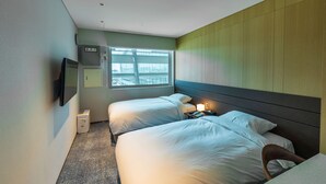Une chambre d’hôtel avec deux lits, une télévision, un bureau avec une lampe et une fenêtre donnant sur un immeuble.