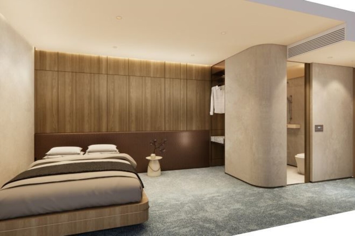 A modern hotel room with a bed, a small side table, and a bathroom visible through an open door.