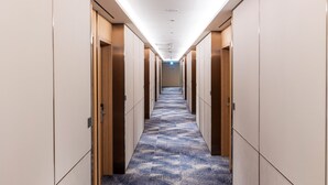 Un couloir d’hôtel avec un sol recouvert de moquette, des portes en bois et un plafond doté d’un éclairage encastré.