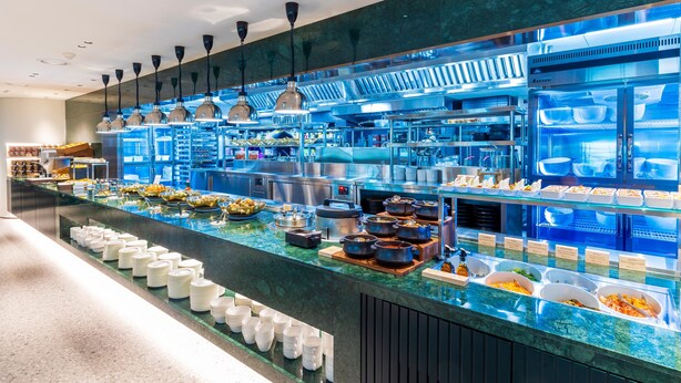 Un buffet proposant différents stands de nourriture et un long comptoir où sont disposées des assiettes et des bols.