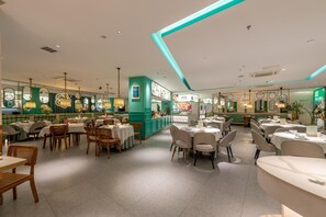 Un restaurant doté de plusieurs tables et chaises, d’un comptoir avec un menu, et d’un mur d’accent de couleur verte.