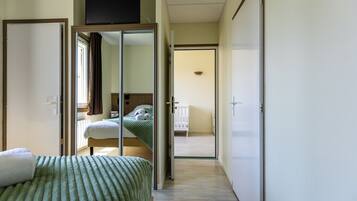 A hotel room with a bed, a TV mounted on the wall, and a sliding door leading to another room.