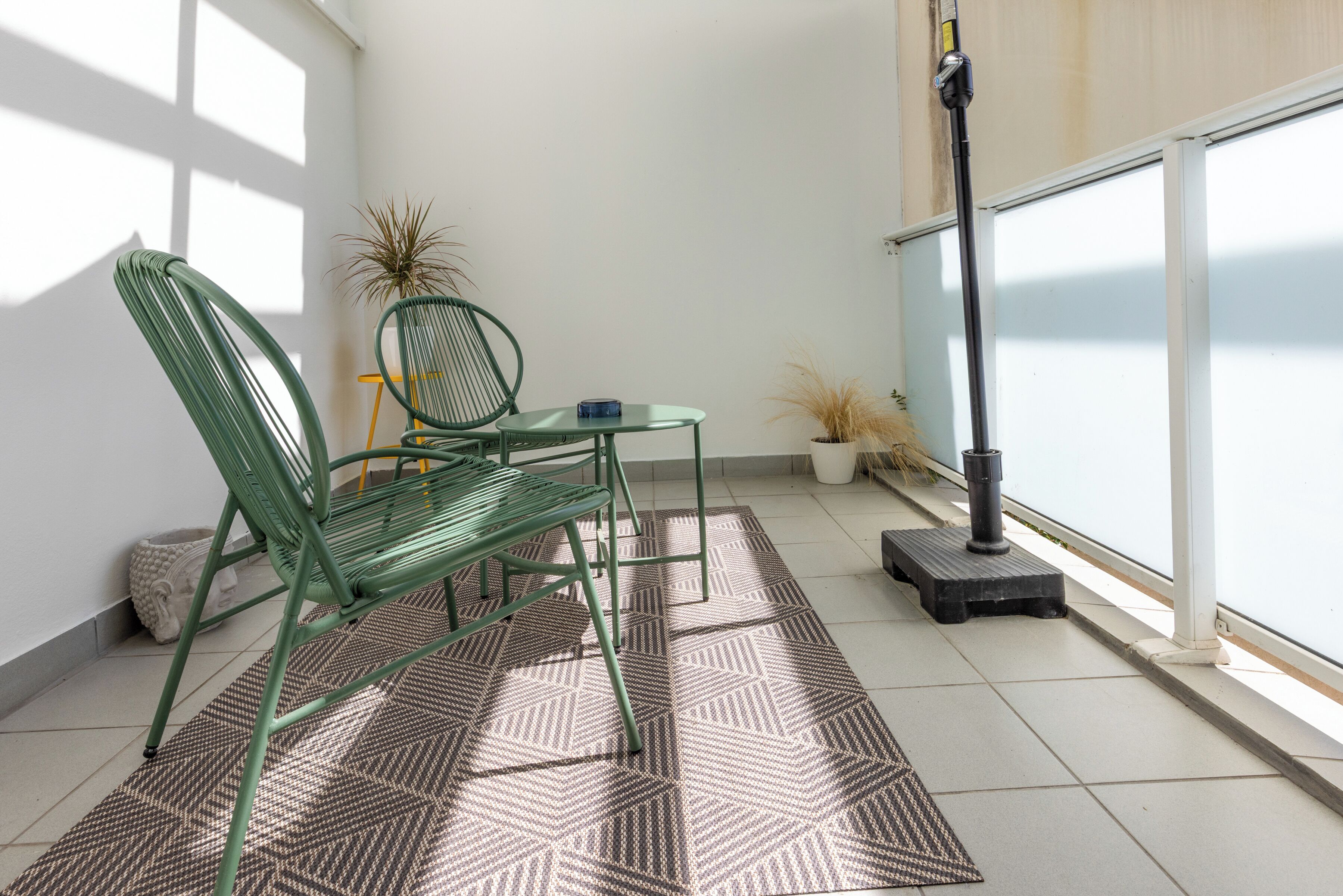 A balcony with a green chair, a small table, and a potted plant.