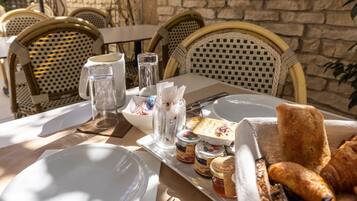 A table set for breakfast with plates, cutlery, a glass pitcher, jars of jam, and bread.