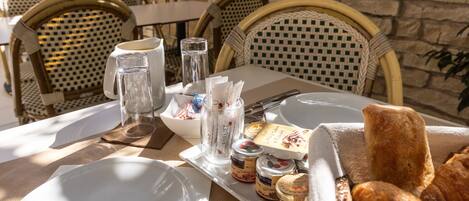A table set for breakfast with plates, cutlery, a glass pitcher, jars of jam, and bread.