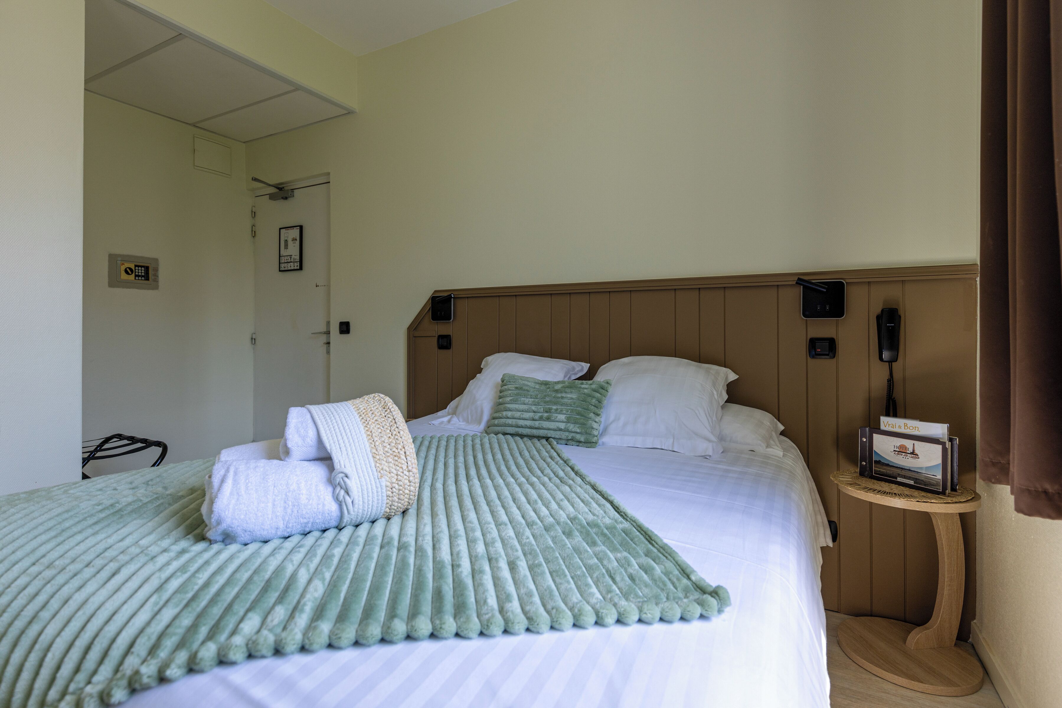 A hotel room with a bed, a bedside table, a wall-mounted phone, and a door.