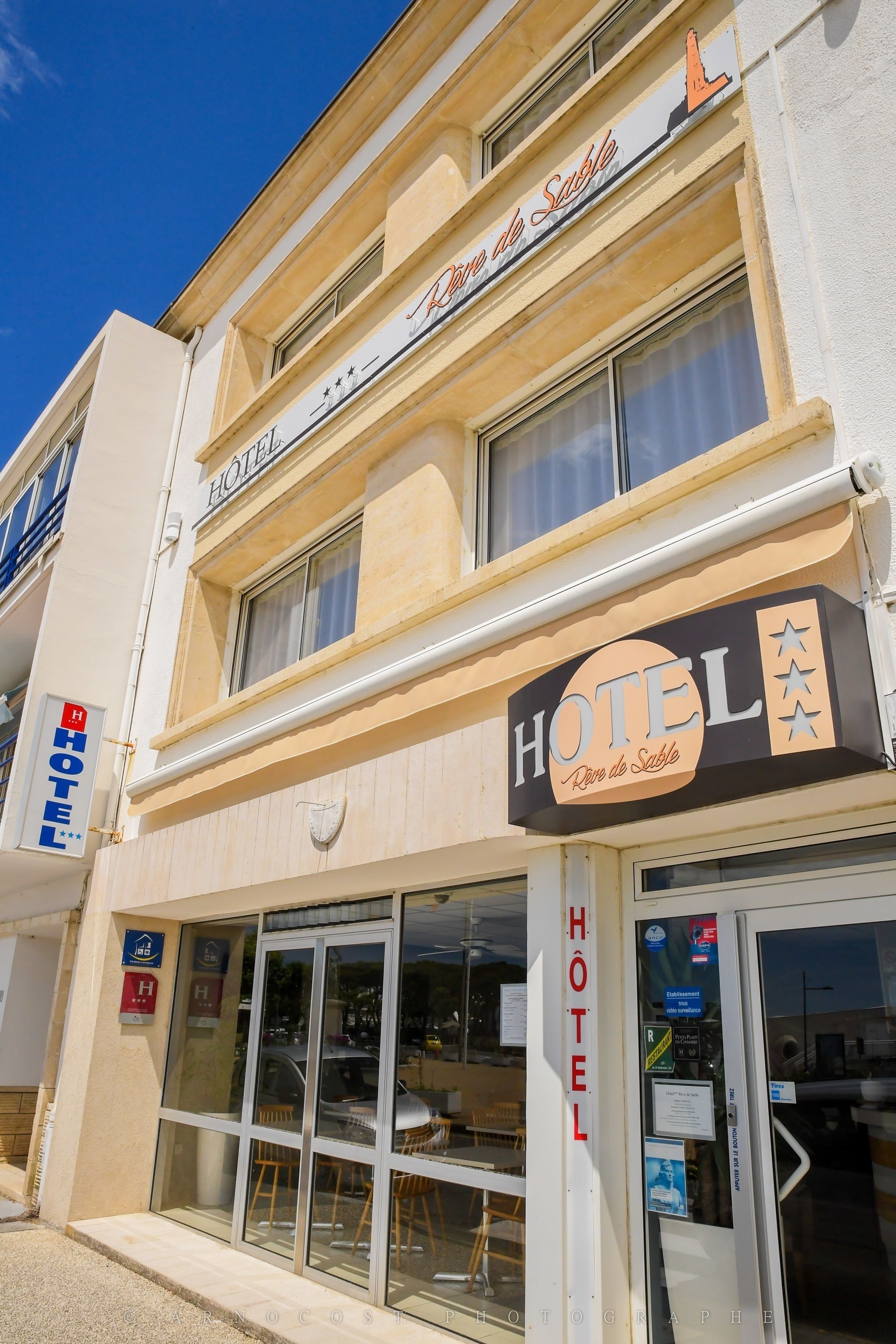 A hotel with a sign reading "HOTEL Dune de Sable" and a visible entrance with glass doors.