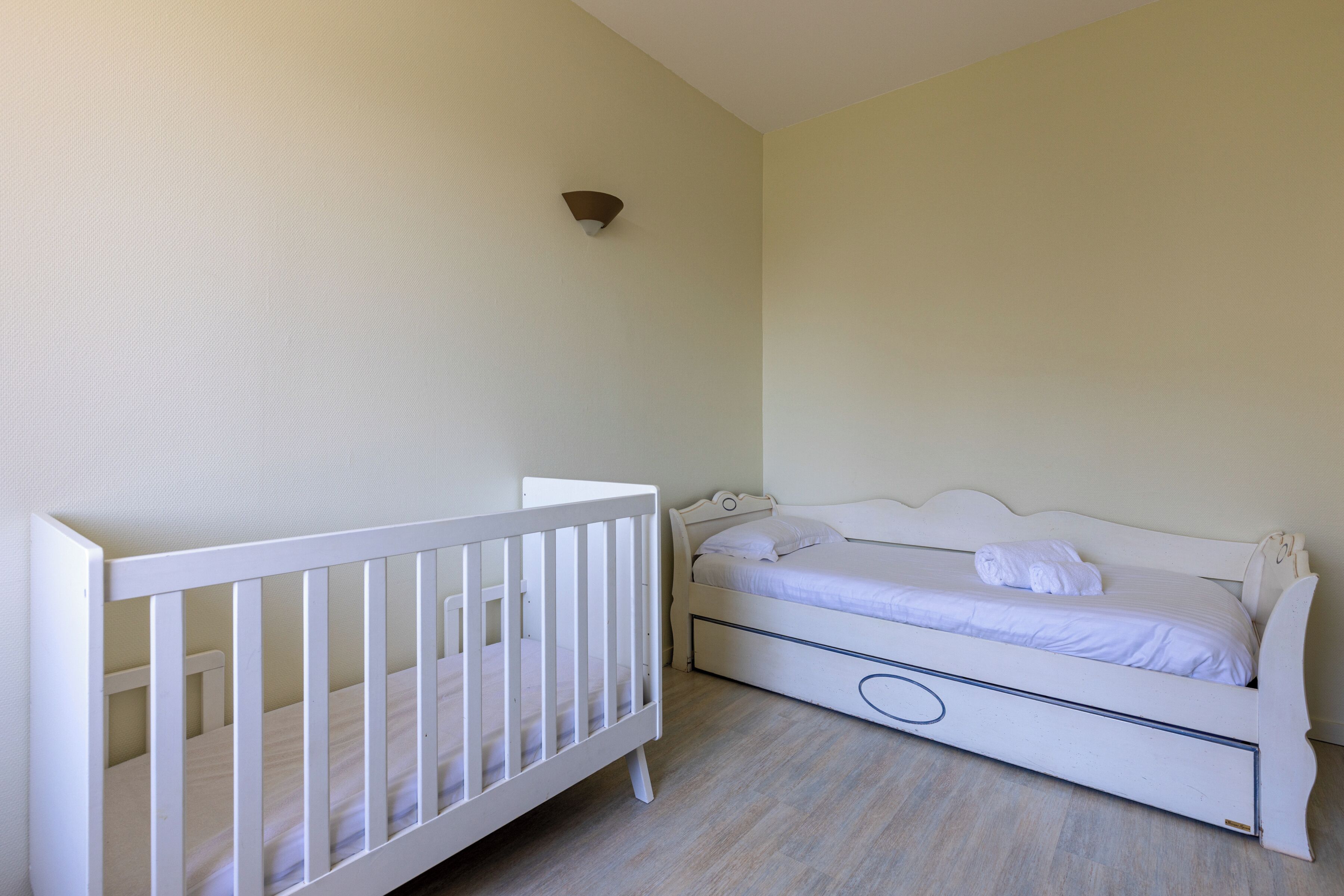 Een kamer met een wit ledikant, een enkel bed met hoofdbord, en een wandlamp.