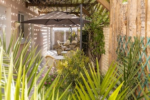 Un espace extérieur aménagé, abrité et doté de mobilier en osier et d’un grand parasol.