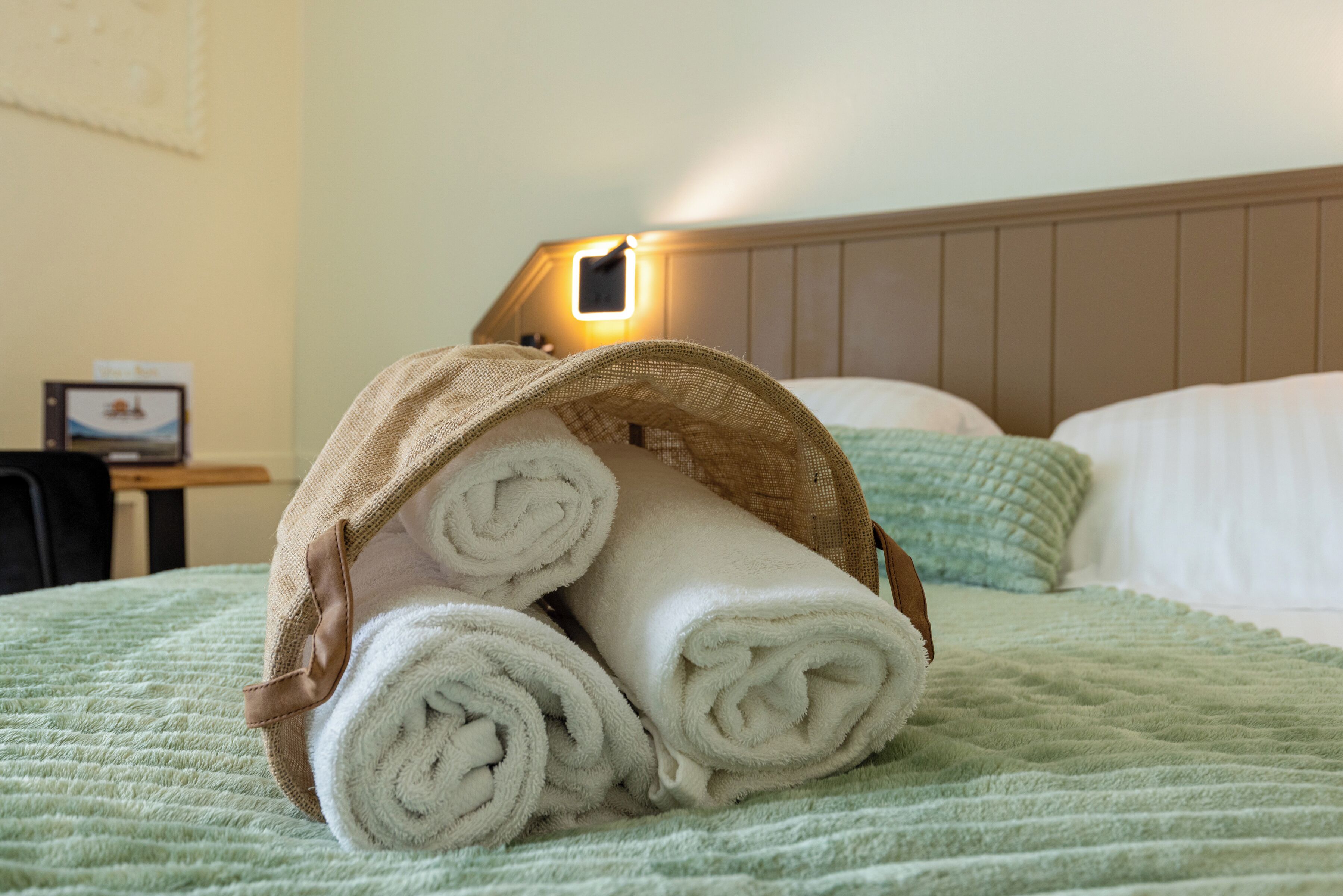 A bed with a green quilt, a headboard, and a lamp on the wall.