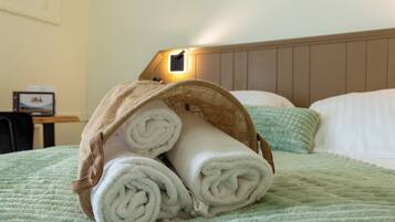 A bed with a green quilt, a headboard, and a lamp on the wall.
