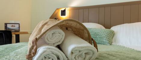 A bed with a green quilt, a headboard, and a lamp on the wall.