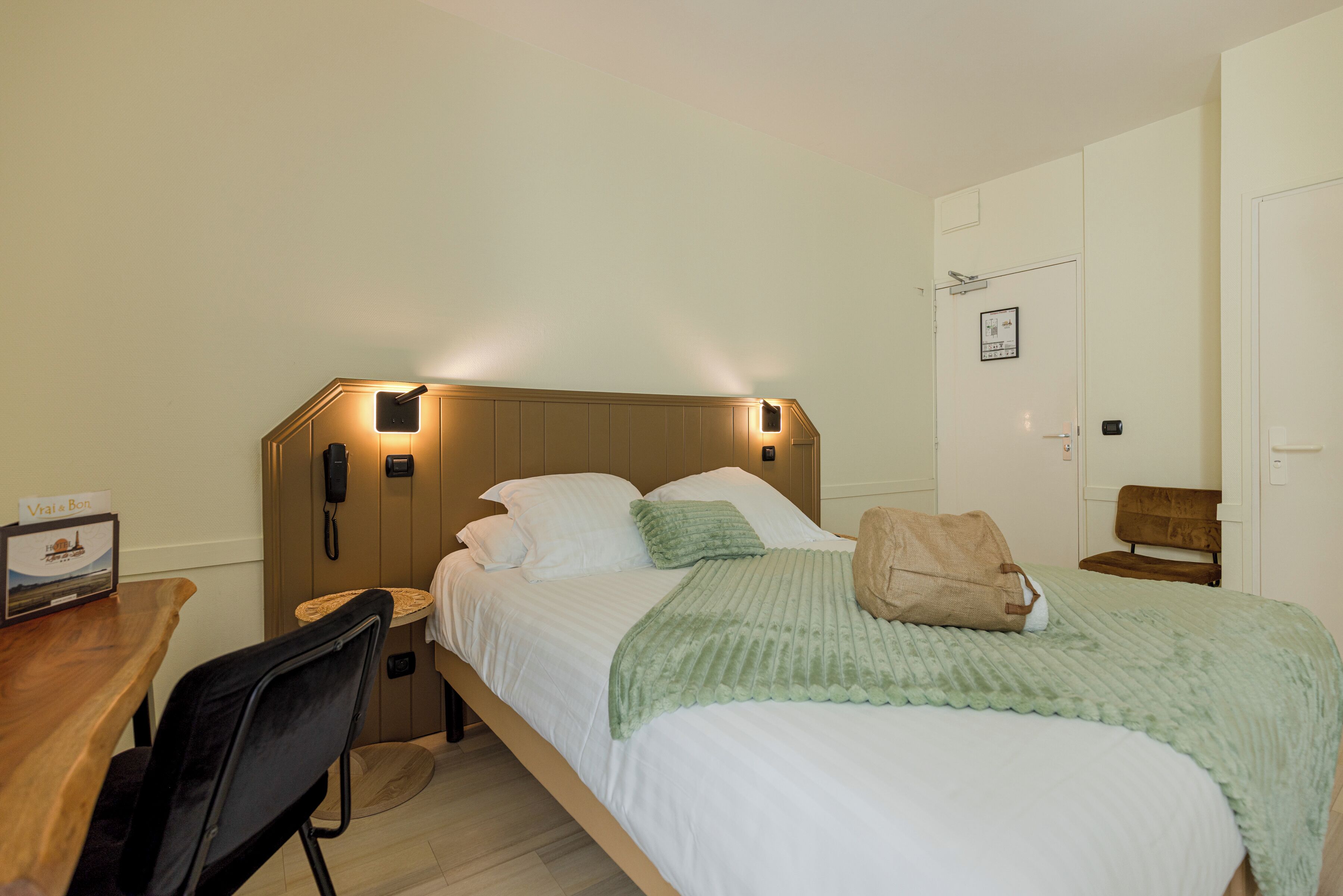Ein Hotelzimmer mit Bett, Nachttisch, Sessel und Schreibtisch mit Stuhl.