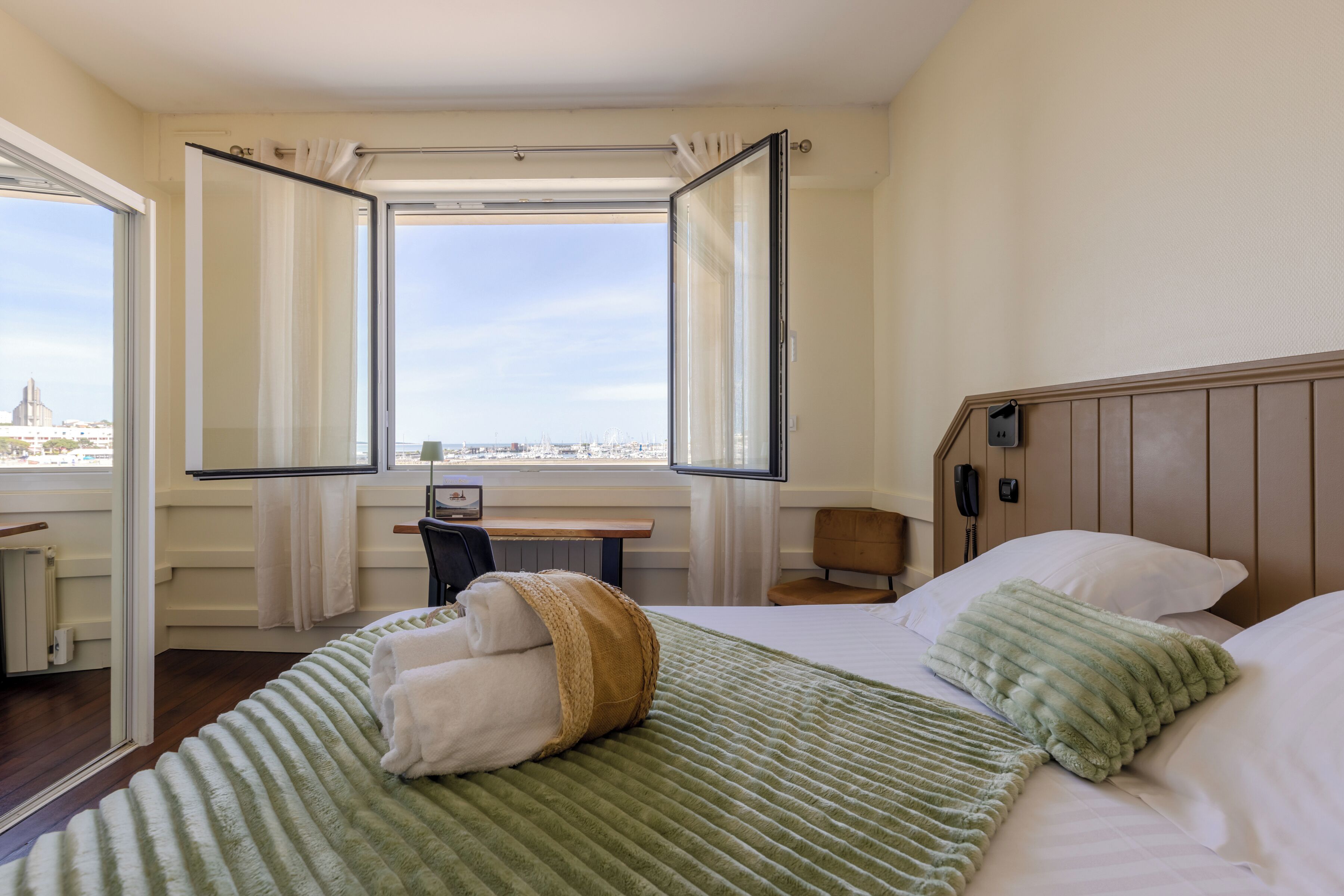 Una habitación de hotel con cama, escritorio, silla y ventana con cortinas.
