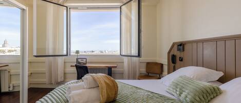 Una habitación de hotel con cama, escritorio, silla y ventana con cortinas.