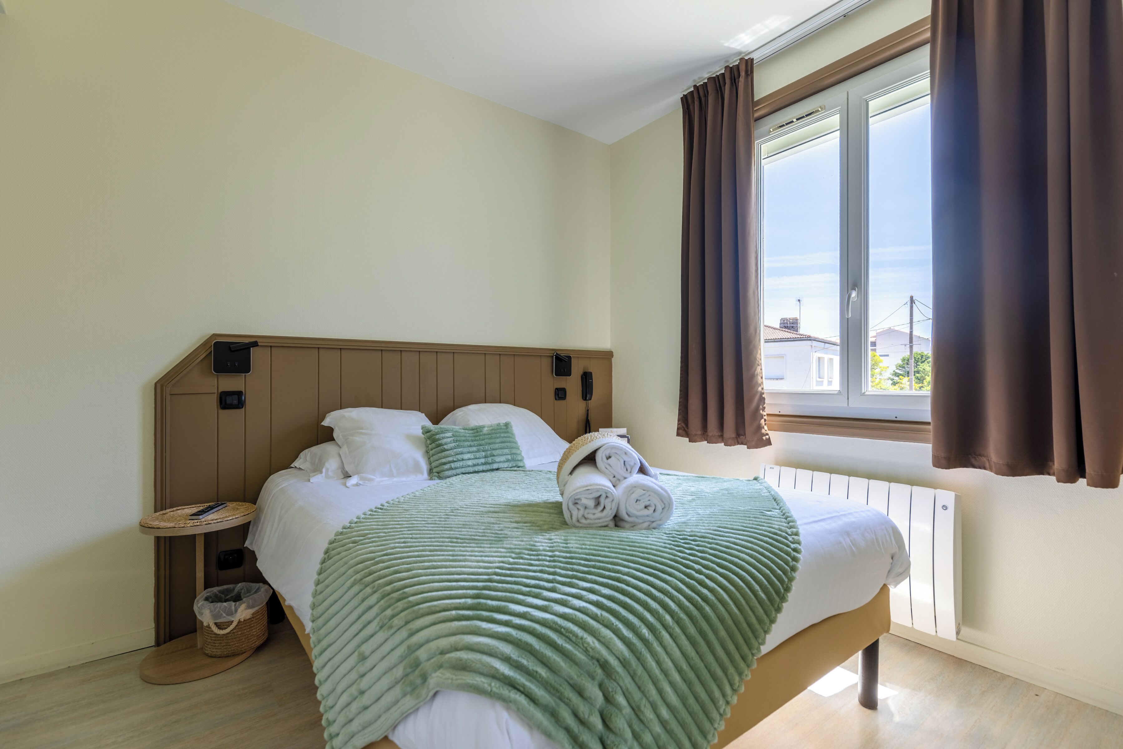 A hotel room with a bed, a bedside table, a lamp, and a window with curtains.