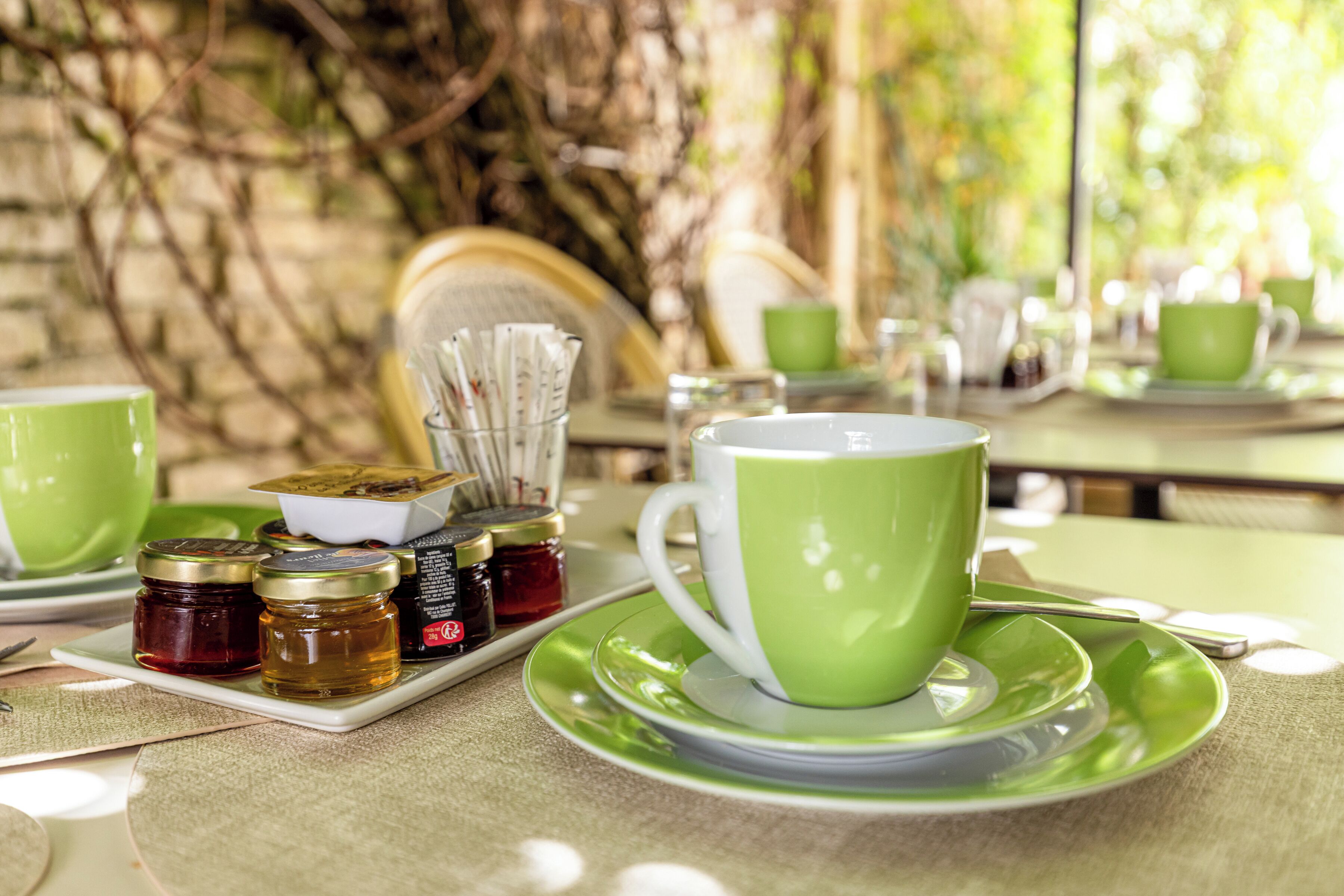 Una mesa dispuesta con vajilla verde, incluyendo una taza y platillo, una bandeja con frascos y una cuchara.