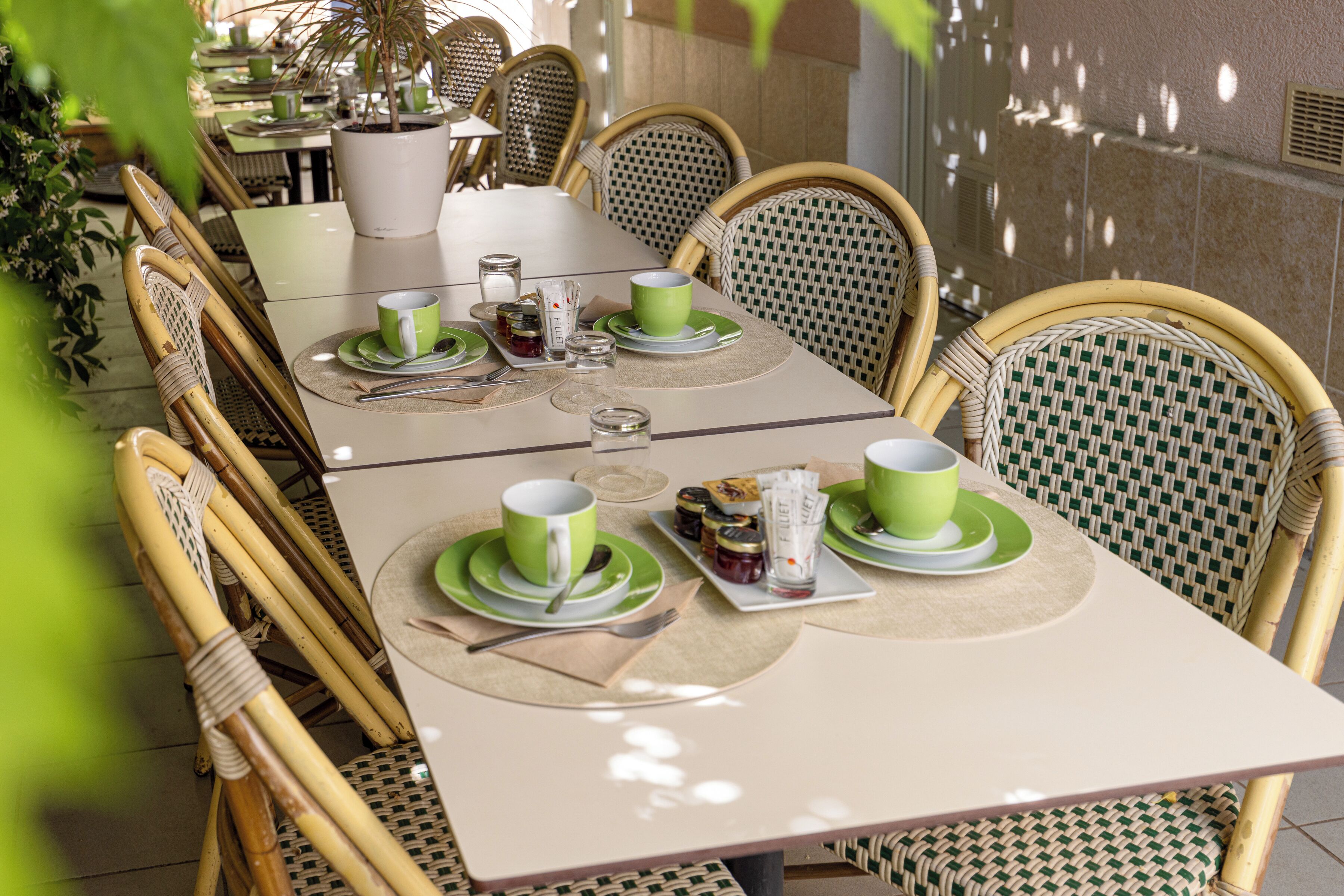 A dining table set with green tableware, surrounded by wicker chairs.