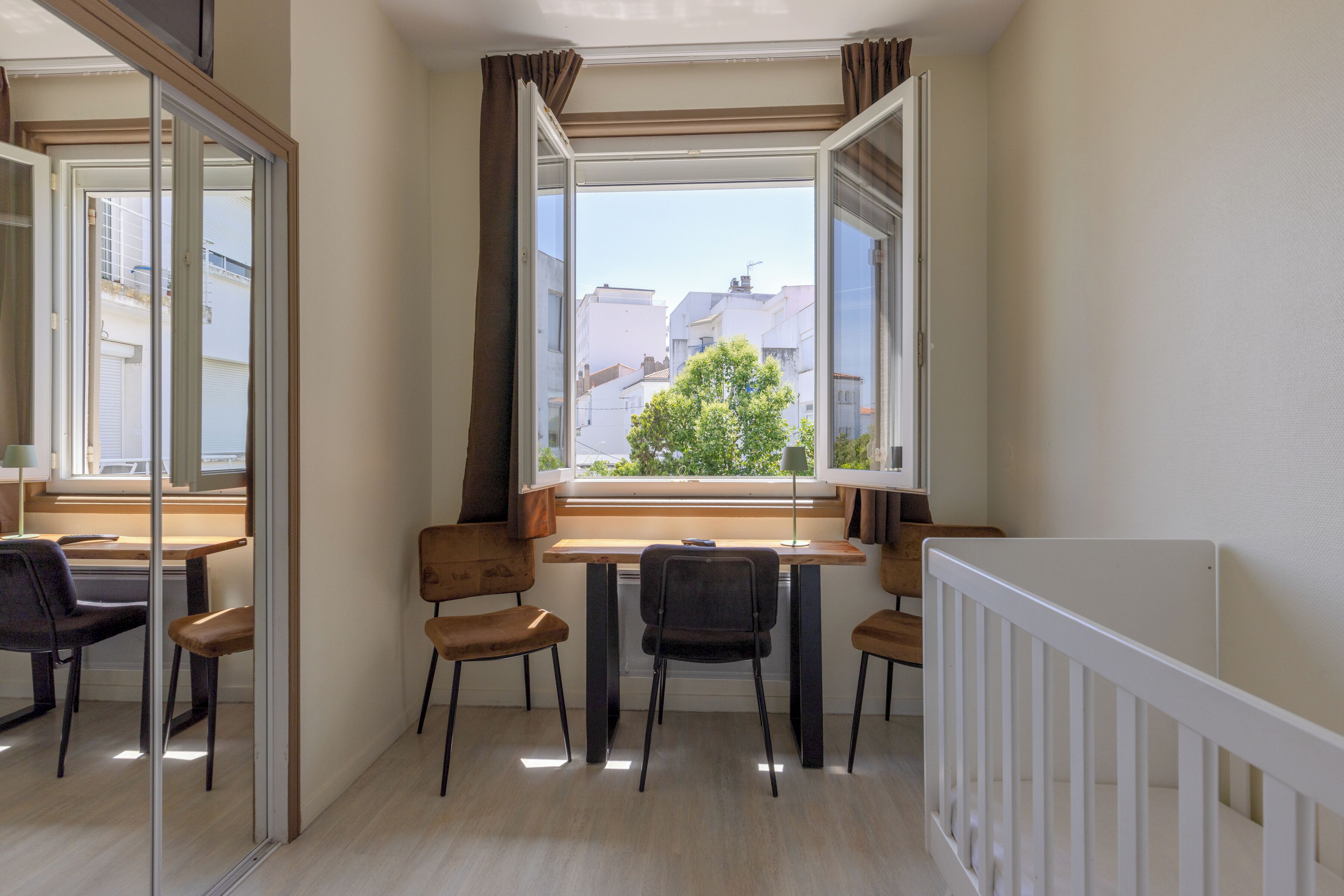 Une pièce comprenant une table à manger, des chaises, une fenêtre avec des rideaux et une rambarde blanche.