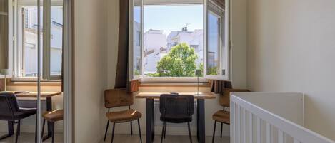 Une pièce comprenant une table à manger, des chaises, une fenêtre avec des rideaux et une rambarde blanche.