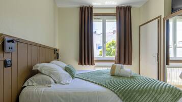 A hotel room with a bed, a telephone, a window with curtains, and a view of the outside.
