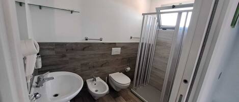 Un bany modern amb rentapousa, vàter, vàter i cabina de dutxa de vidre.