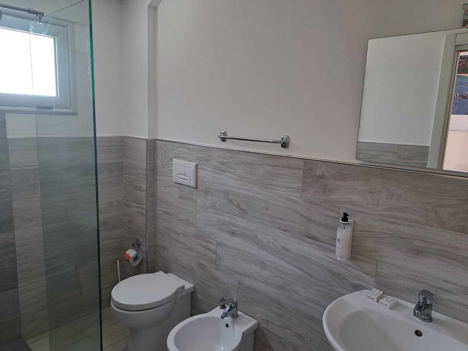 Un bagno moderno con box doccia in vetro, un water e due lavandini.