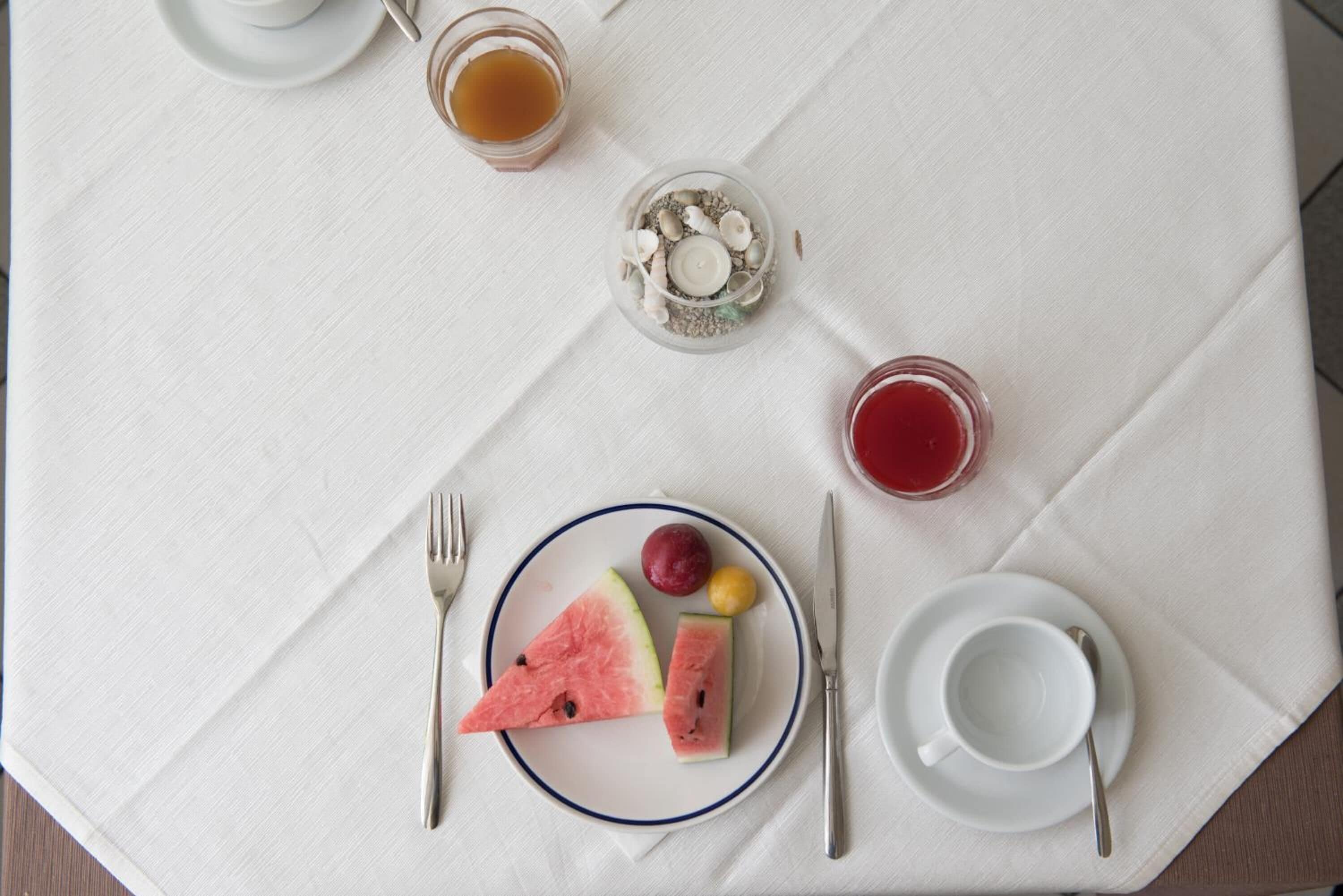 Una colazione servita con anguria, una tazza di tè e un bicchiere di succo su una tovaglia bianca.