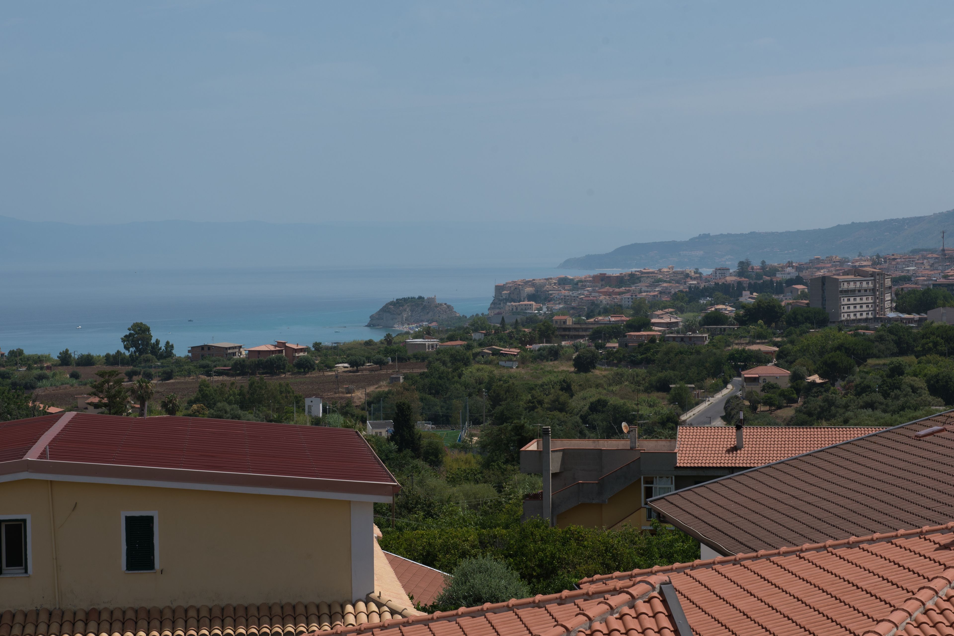 A coastal town with terracotta-roofed buildings, a prominent rocky outcrop, and a view of the sea.